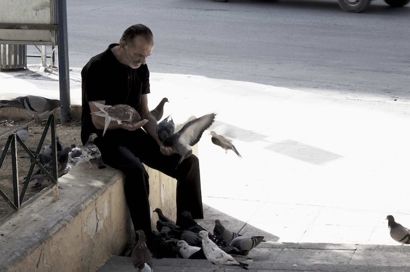 Photographie d'un homme entouré de pigeons qu'il nourrit